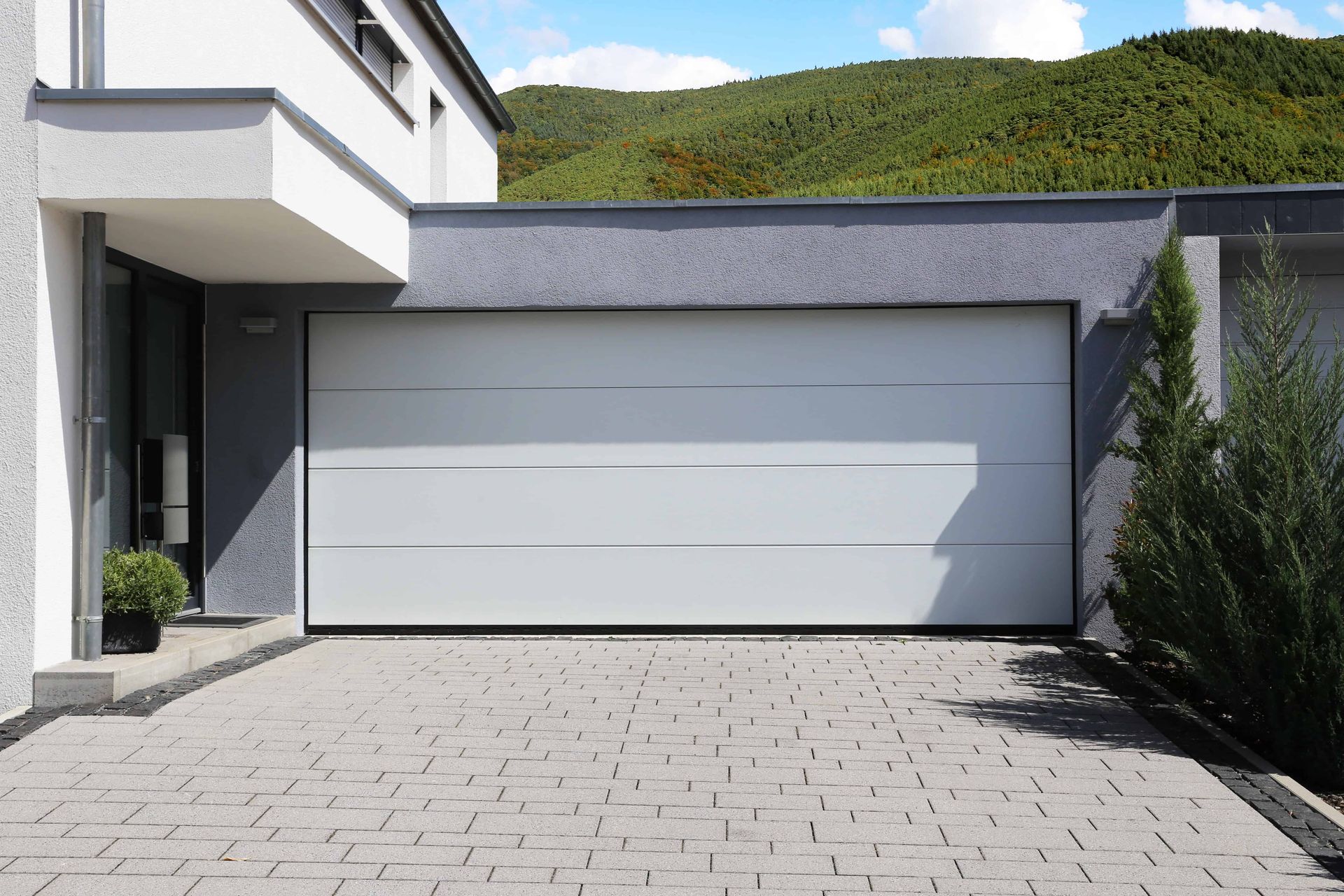 White garage door on a modern house with a paved driveway and greenery.