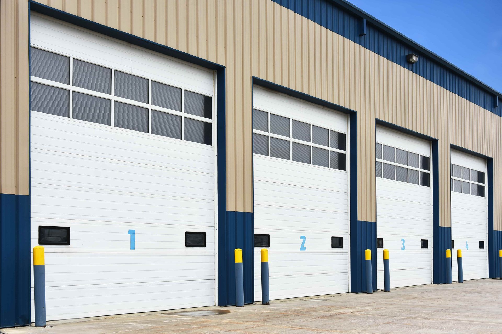 Four white garage doors with windows, labeled 1-4, on a tan building with blue trim.