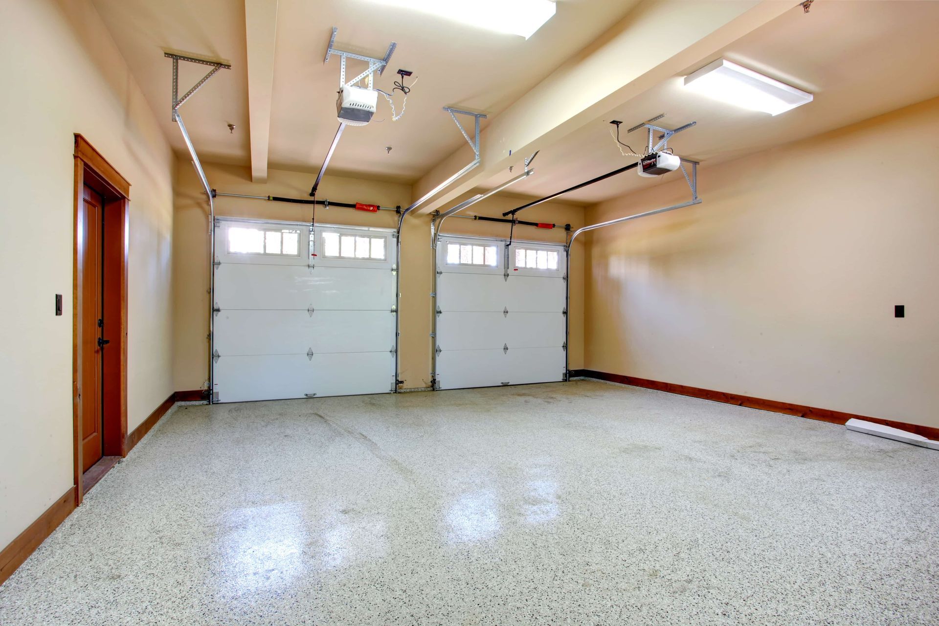 Empty two-car garage with white doors, speckled flooring, and beige walls.