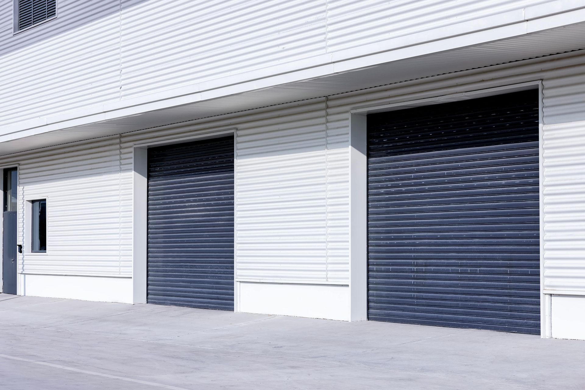 Exterior of a commercial building with two closed gray rolling shutter doors.