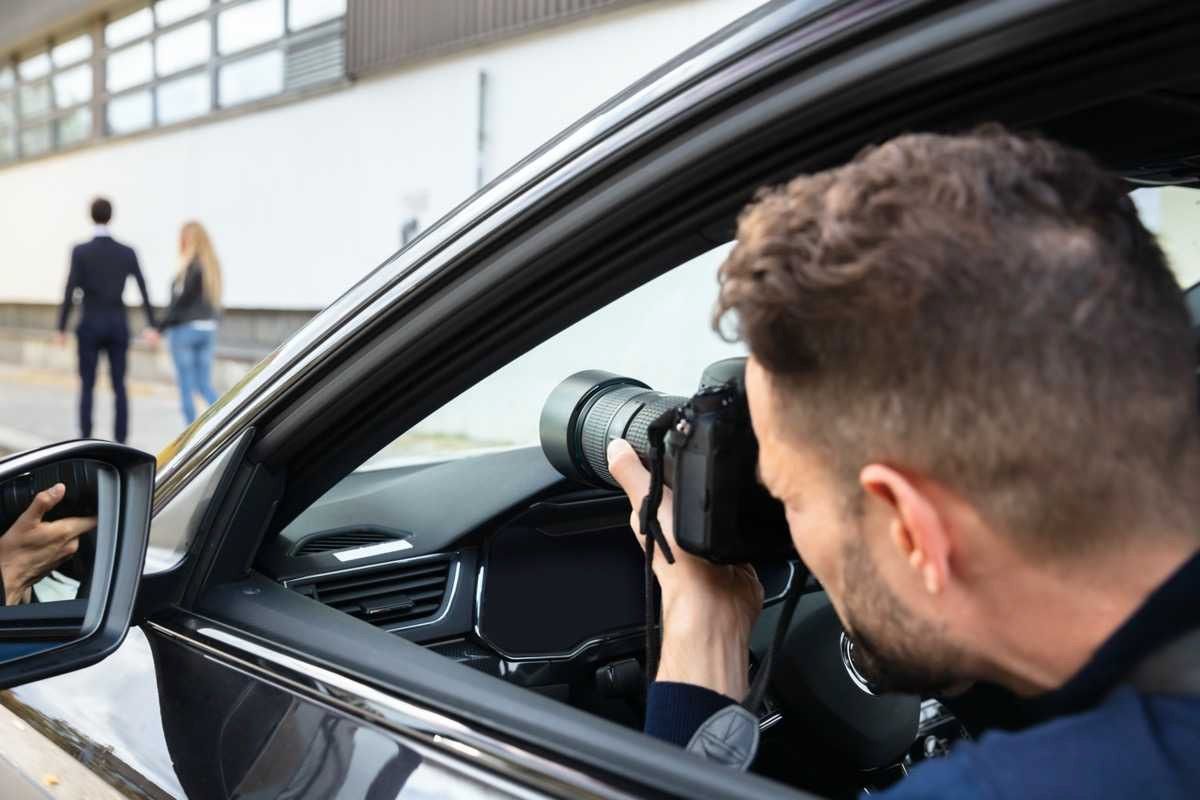 Paparazzo in a car taking photo of a couple walking.