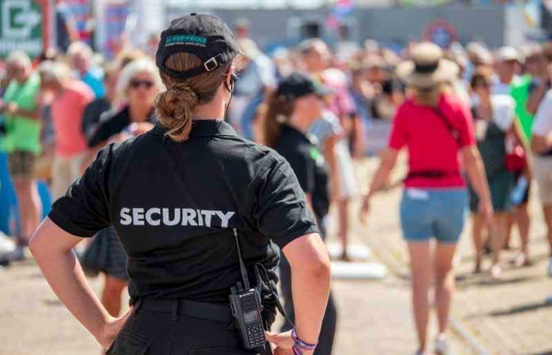 Security guard in black uniform surveying a crowd at an outdoor event.