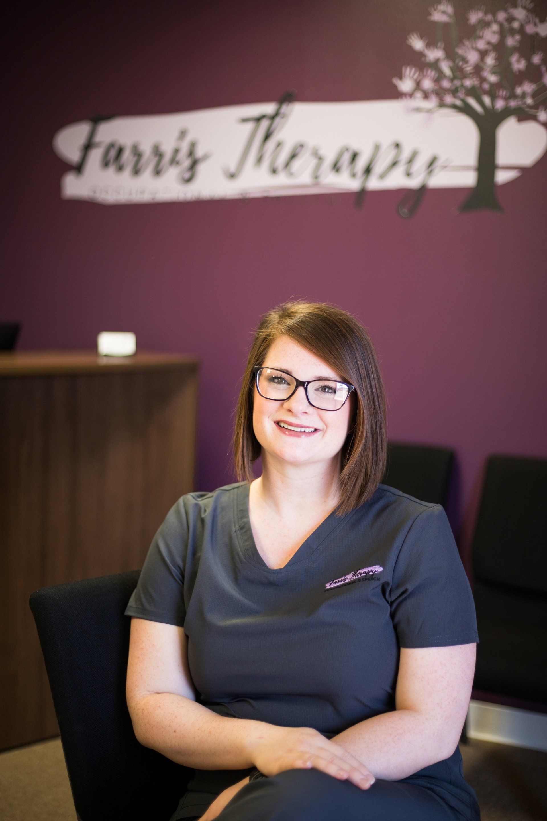 A woman is sitting in a chair in front of a purple wall.