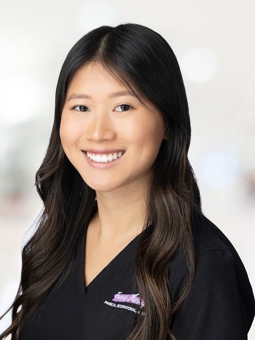 A woman in a black scrub top is smiling for the camera.