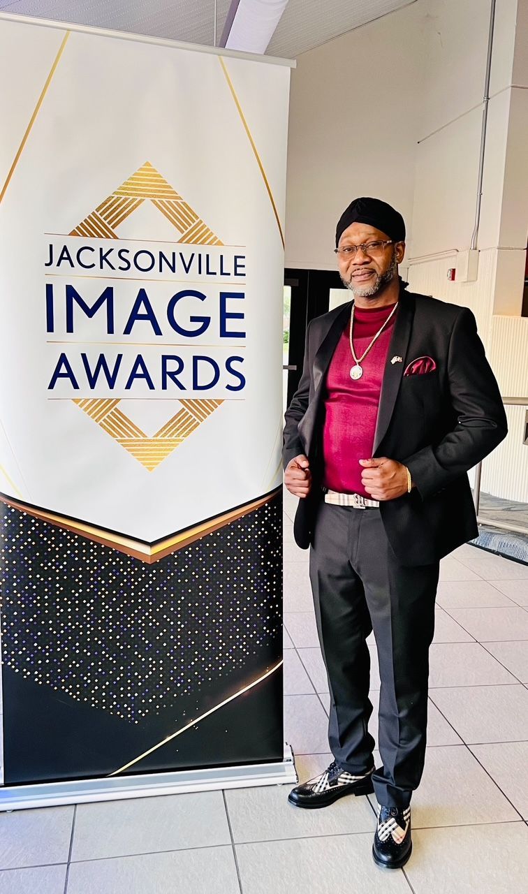 A man in a suit is standing in front of a sign for the jacksonville image awards.