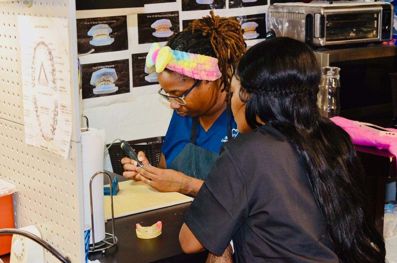 Two women are sitting at a table working on a denture