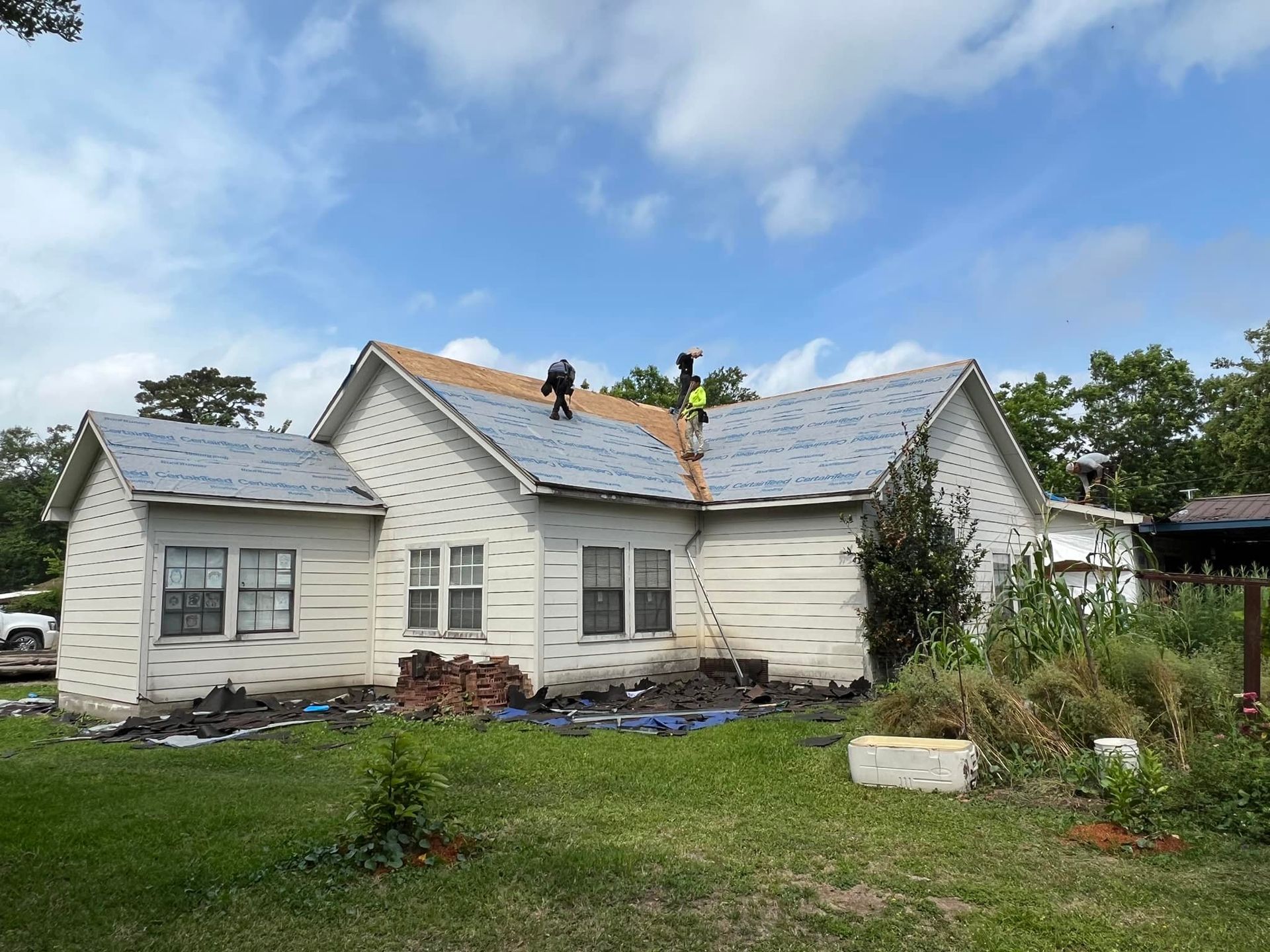 Workers installing shingles on a white house roof under a cloudy sky.