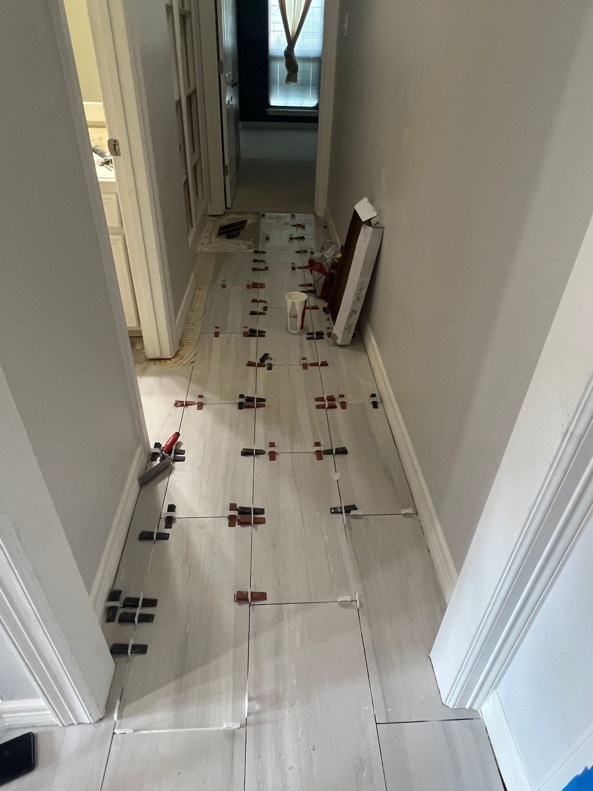 Hallway with gray tile flooring installation in progress, tiles set with spacers.