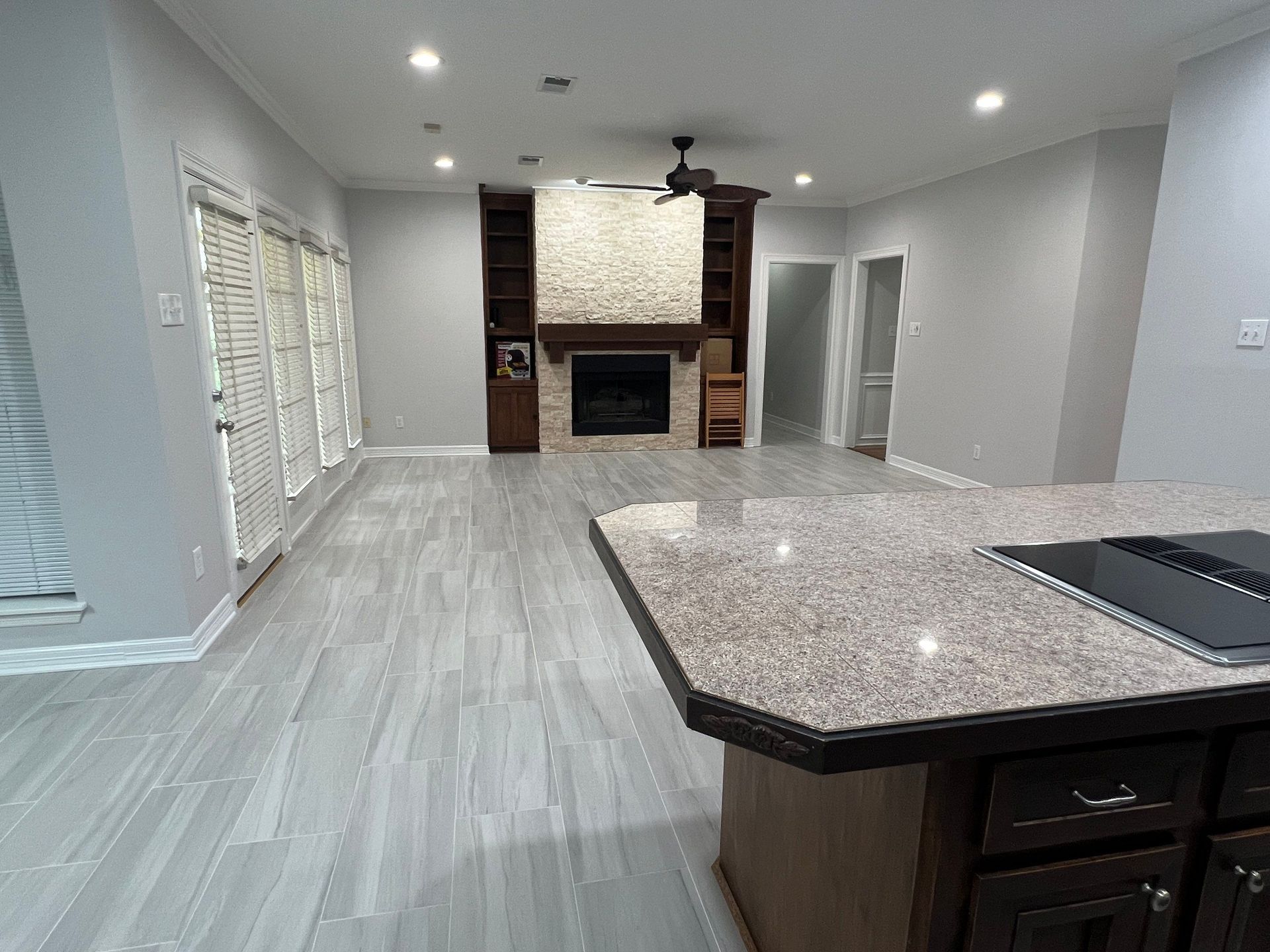 Spacious living room with gray tiled floor, fireplace with built-in shelves, and kitchen island.