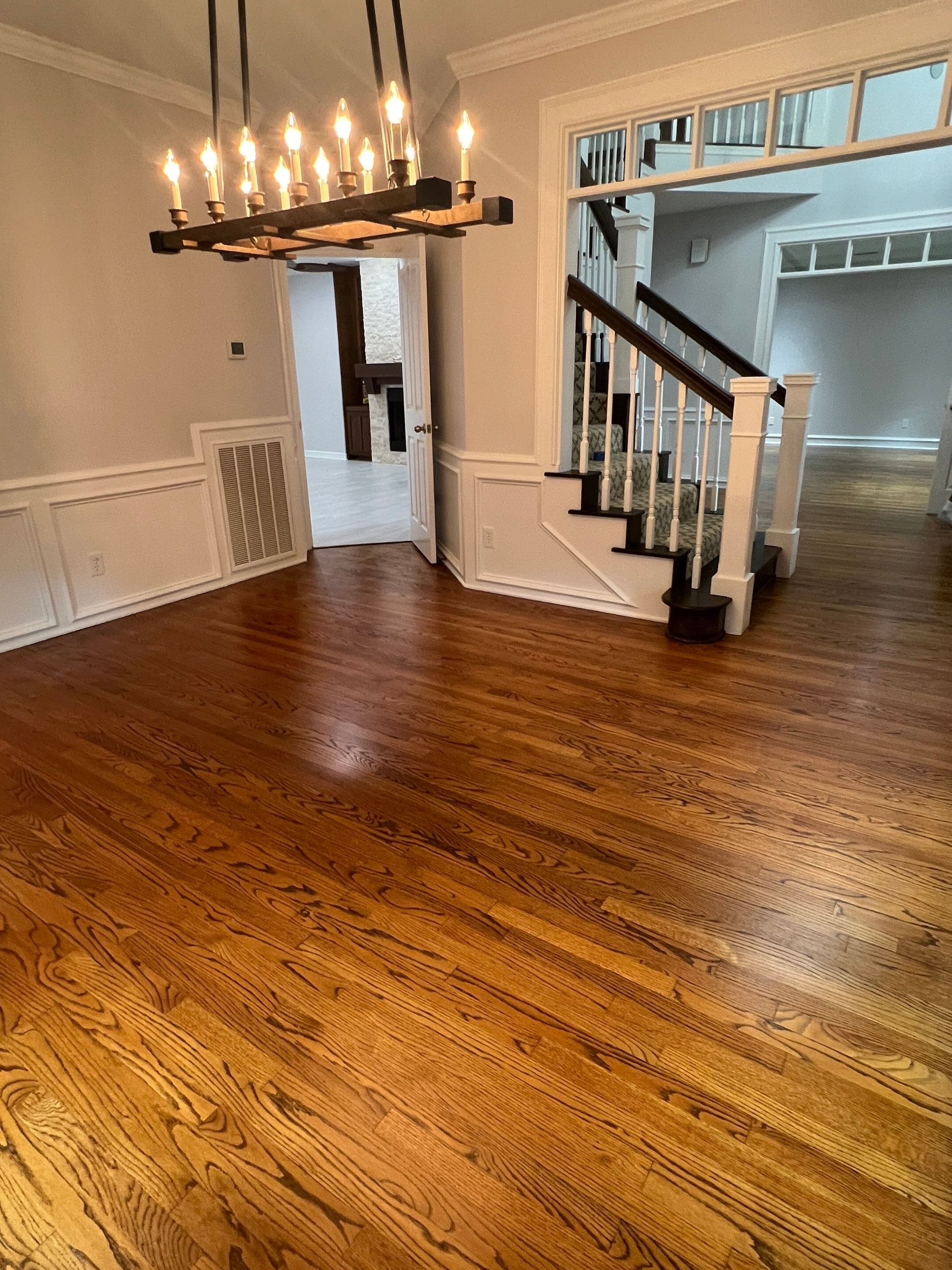Wooden floor in dining room, with staircase and doorway leading to other rooms, chandelier overhead.