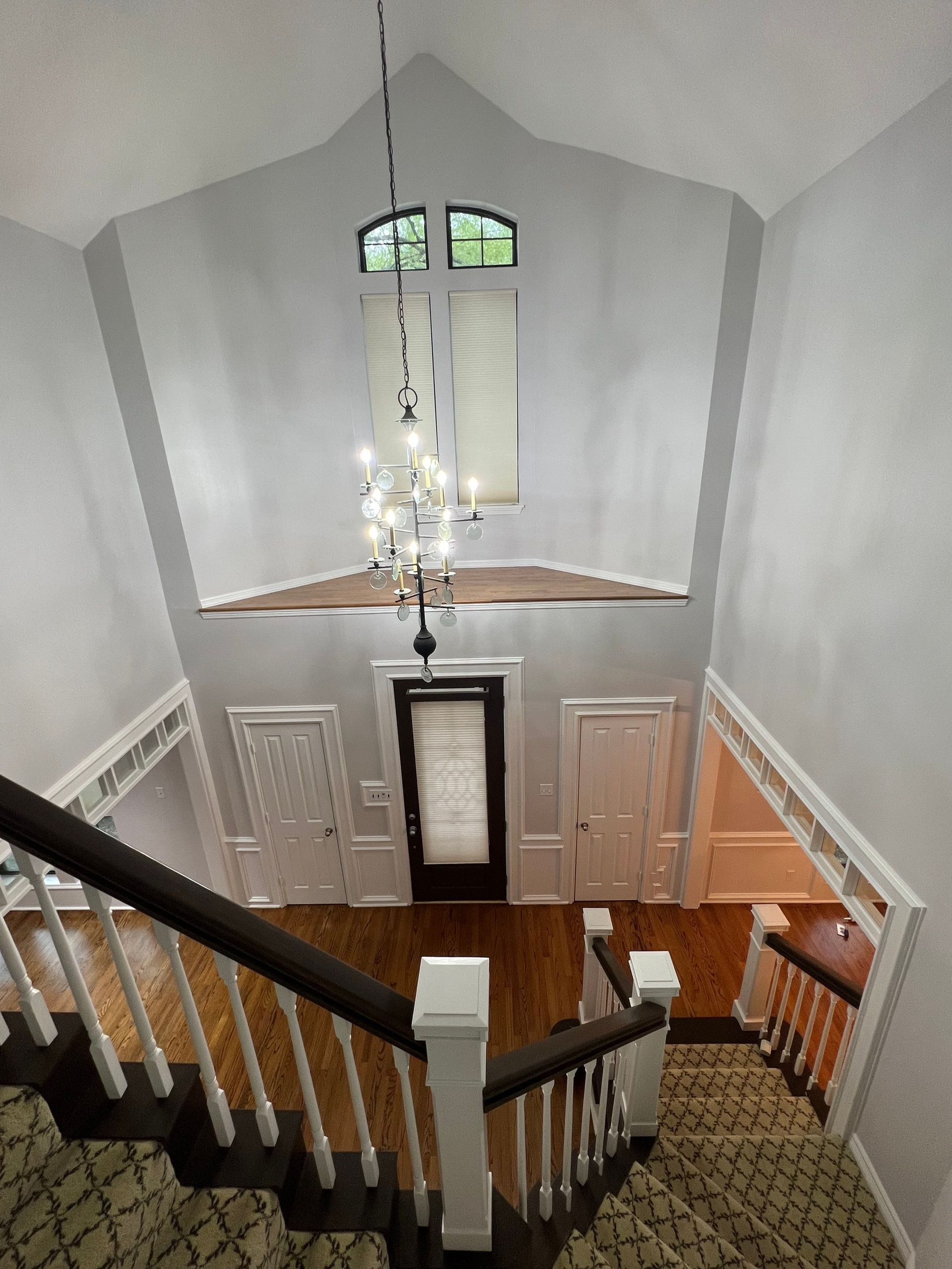 Staircase leading to a two-story foyer with a chandelier, front door, and white walls.