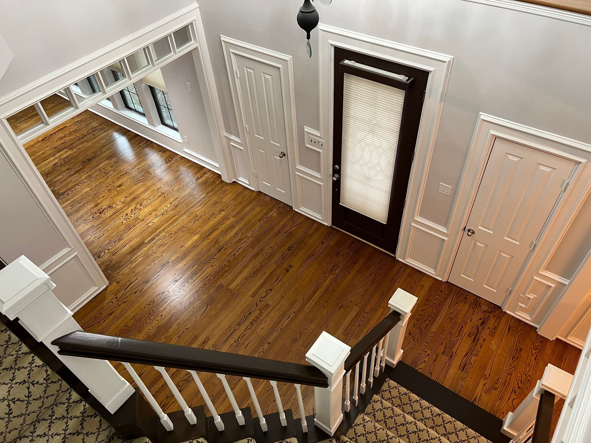 Overhead view of a house entry with hardwood floors, white trim, and a dark brown door. Staircase visible.