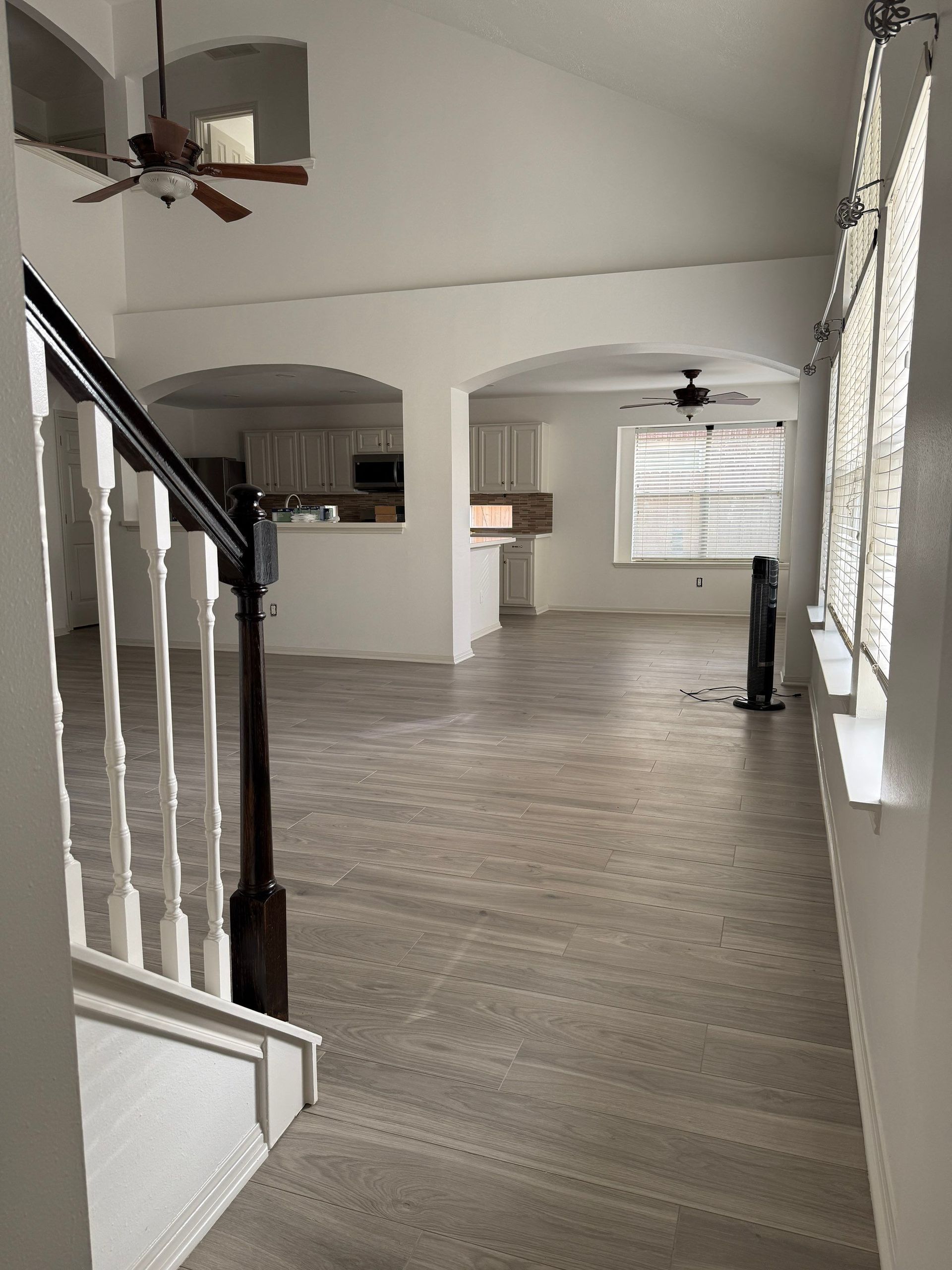 View from a staircase landing into a bright, open-plan living area with arched doorways and a kitchen in the distance.