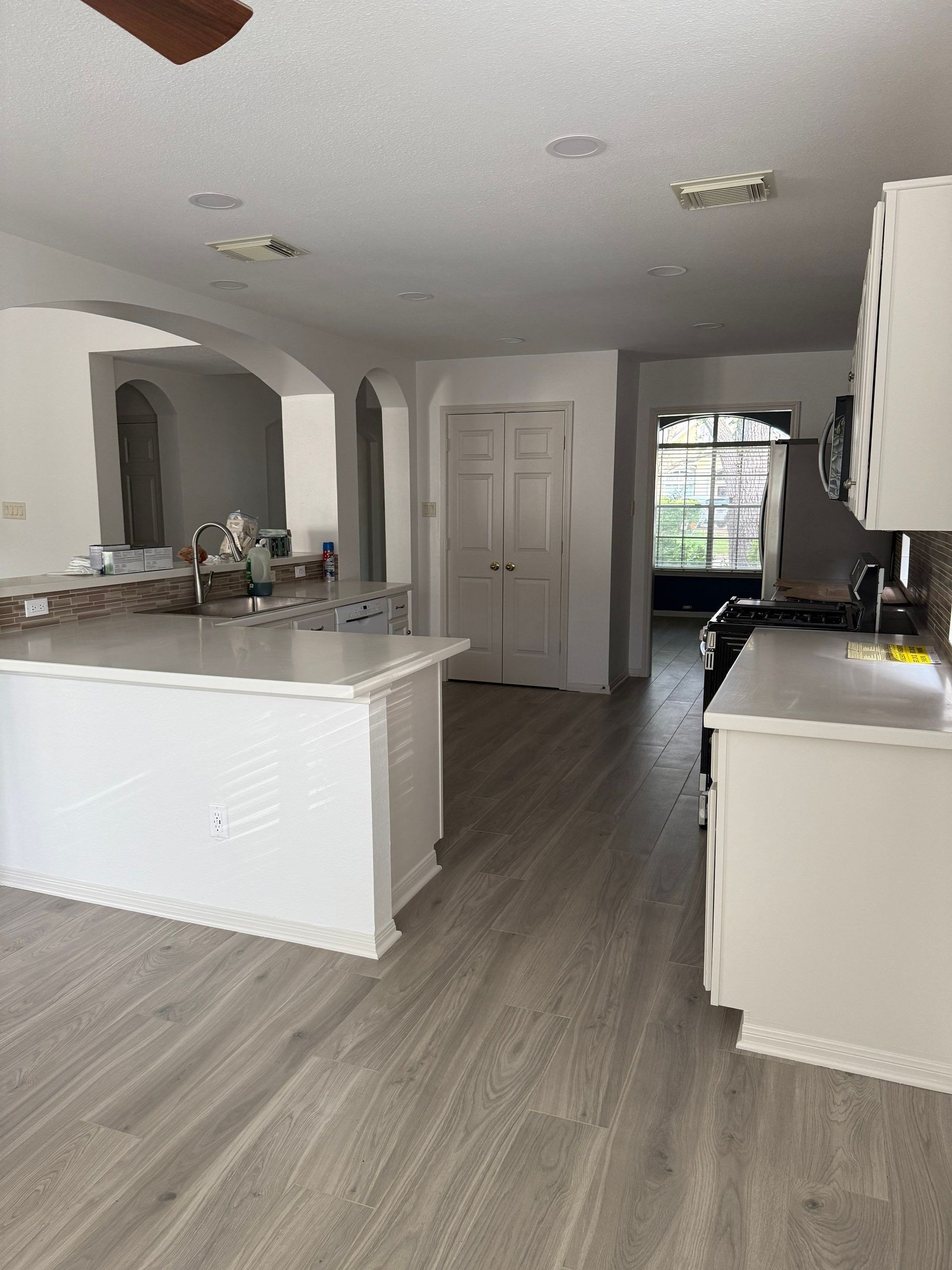Spacious kitchen with white cabinets, island, and light wood-look flooring. Arched doorways lead to other areas.