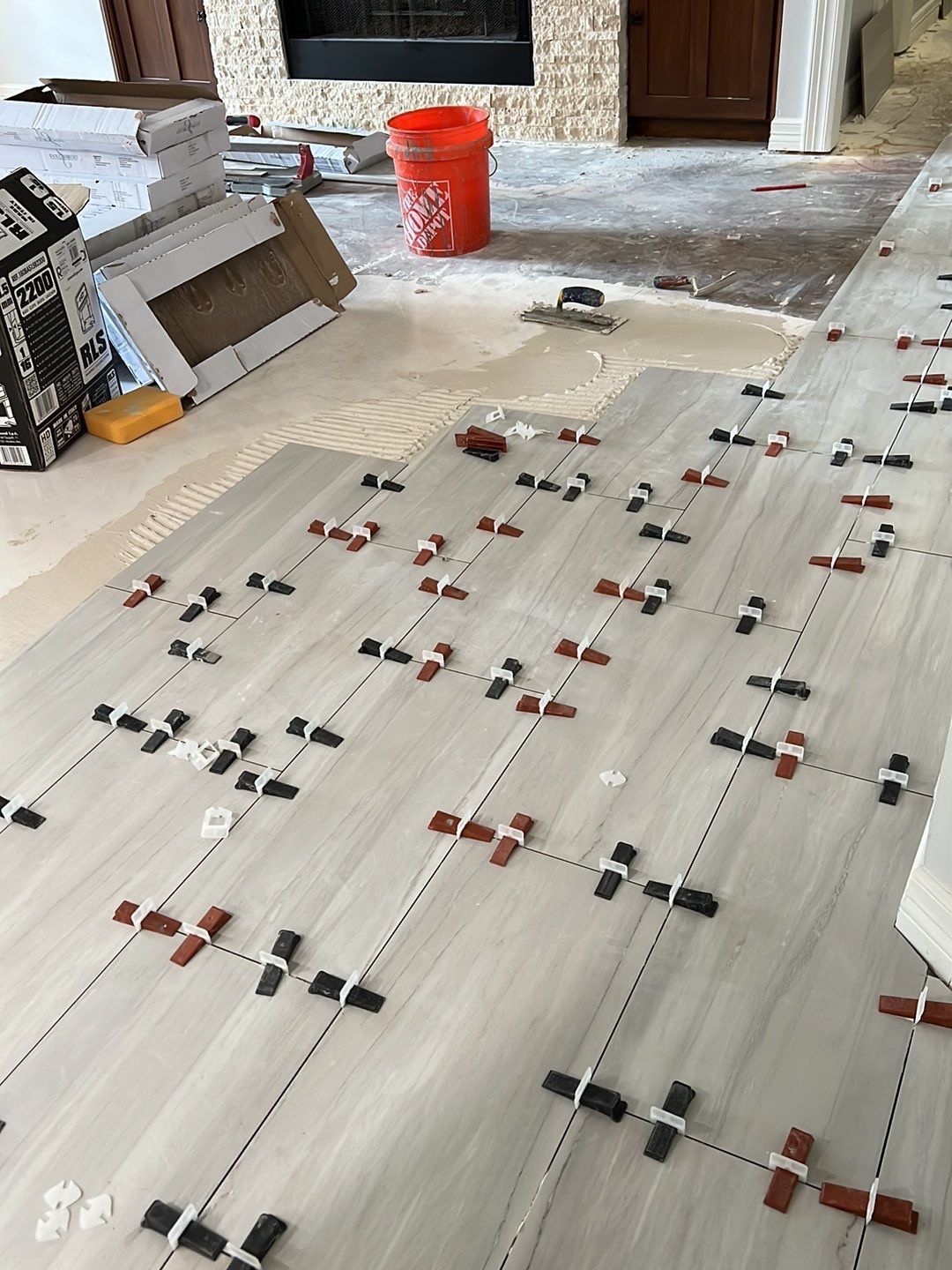 Floor tiling in progress; large, light-colored tiles are being laid with spacers and leveling clips.