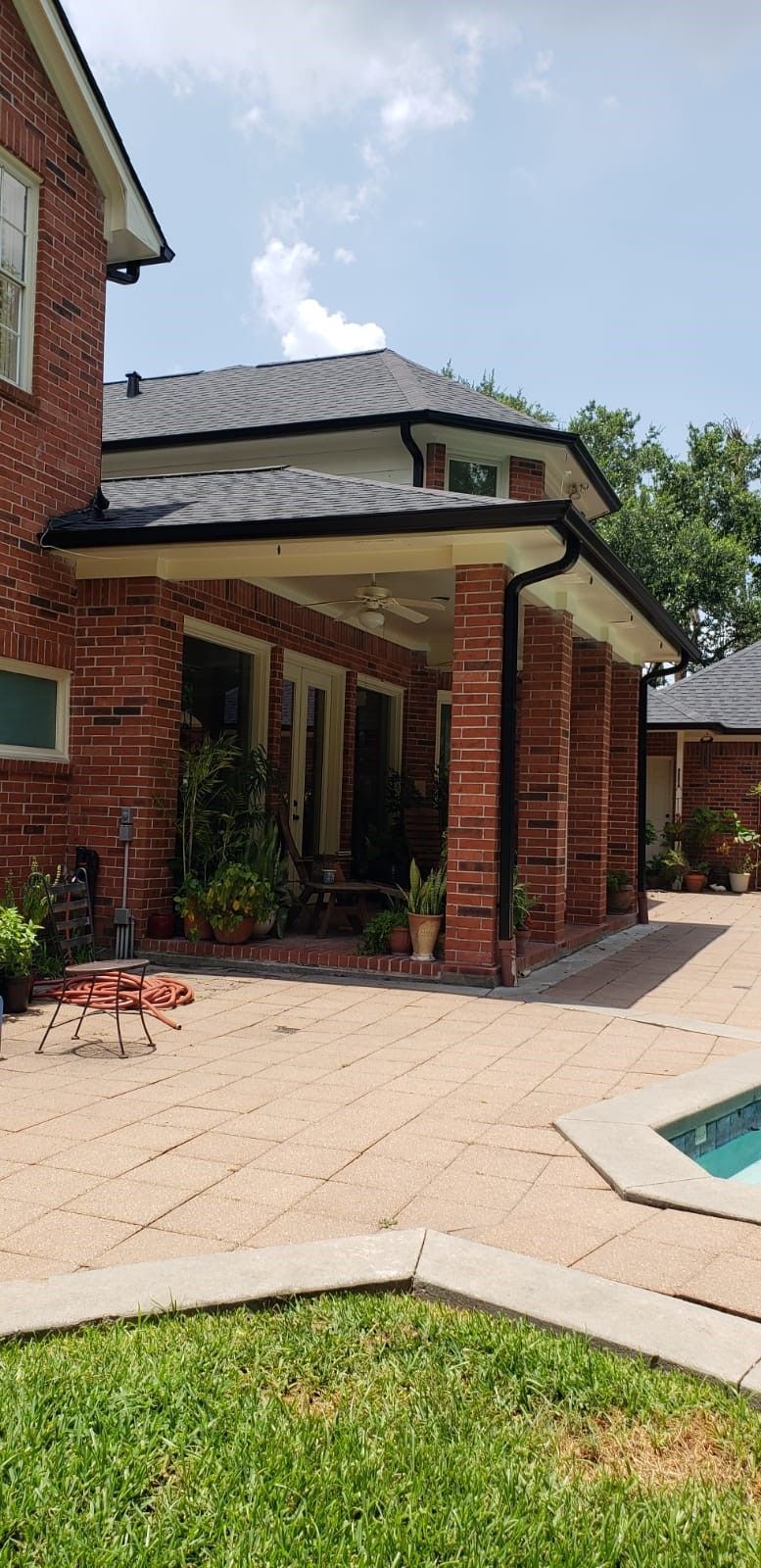 A brick house with a covered porch and a pool in the backyard on a sunny day.