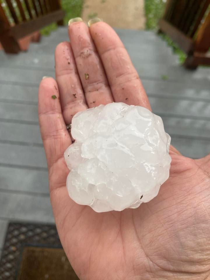 Person's open hand holding a large, jagged hailstone. The hailstone is white and translucent.