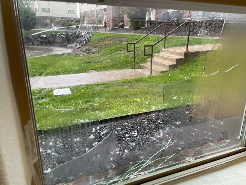 Broken window with shards visible, overlooking a green grassy area with steps and a railing.