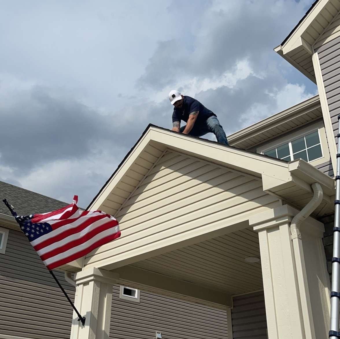 A Former Marine is working on the roof of a house next to an American flag