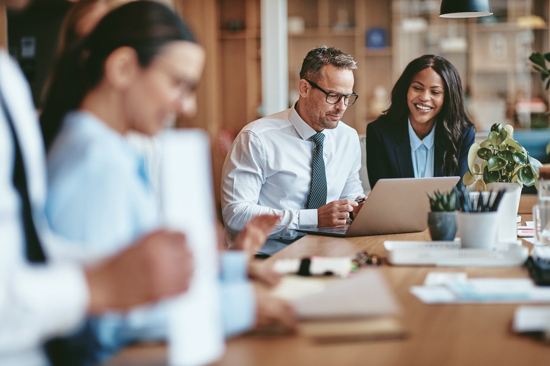 A group of business people are sitting around a table looking at a laptop.