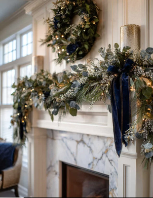 Fireplace mantel decorated with garland, wreath, and blue velvet bows.