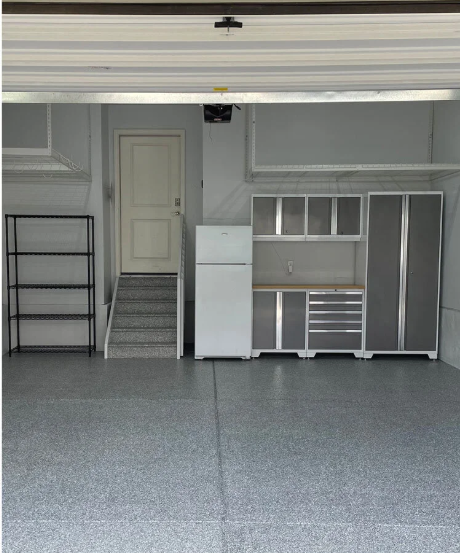 Grey garage interior with epoxy floor, cabinets, refrigerator, shelving, and door.