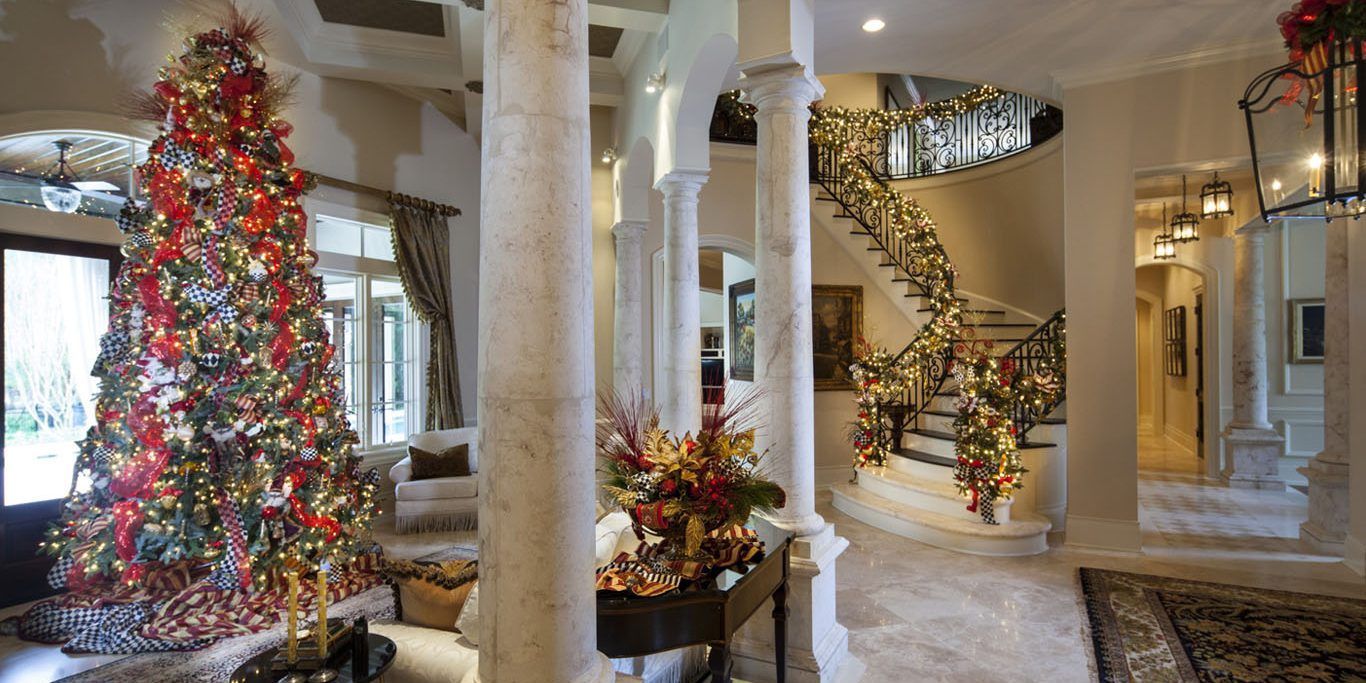A festive foyer with a large decorated Christmas tree and garland-adorned staircase.