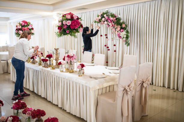People decorate a banquet table with pink flowers.