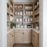 A well-organized pantry with light wood shelves, baskets, and glass jars filled with various food items.