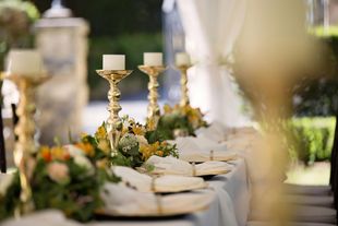 Elegant table setting with gold candle holders, floral arrangements, and folded napkins.