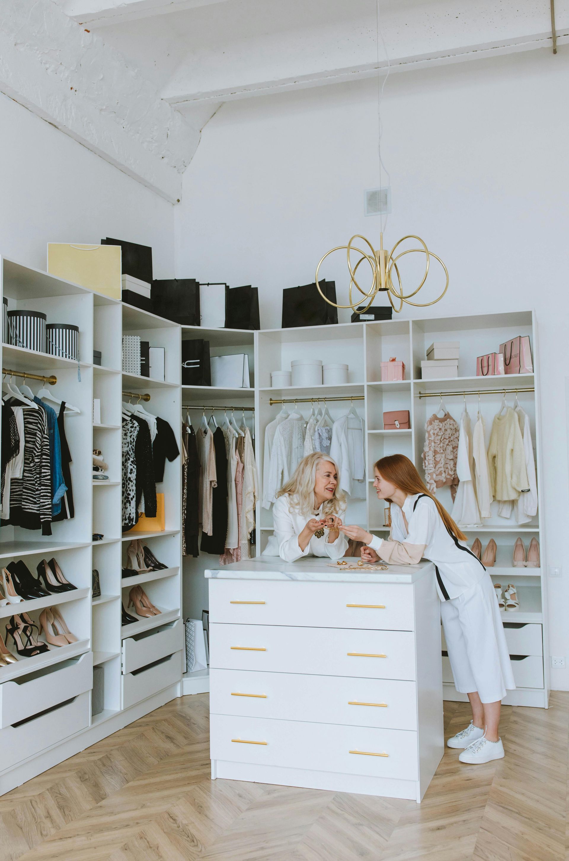 Two people, one blonde and one redhead, in a white walk-in closet, holding glasses, smiling.