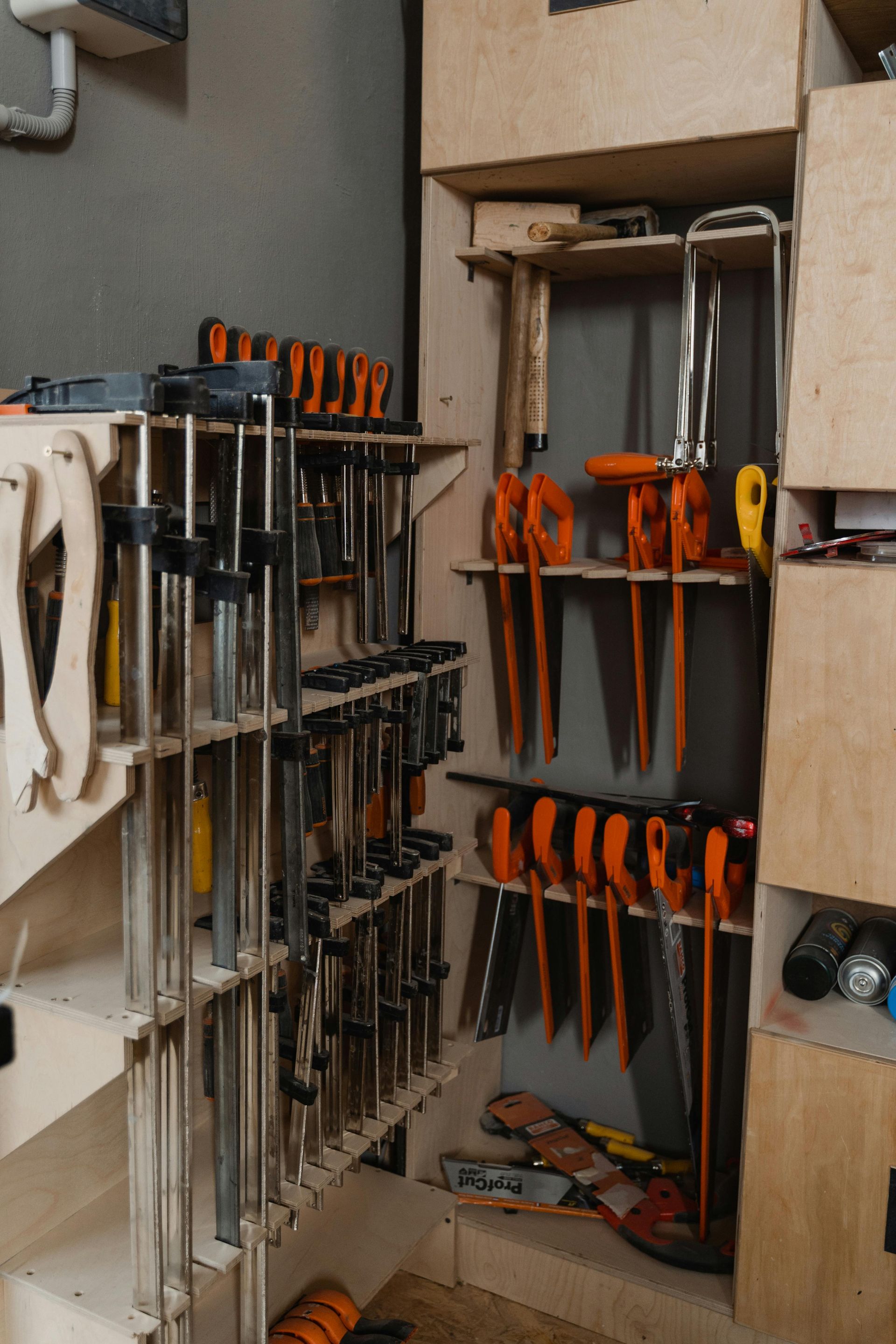 Clamps organized on shelves in a wooden workshop, with orange and metal tools.