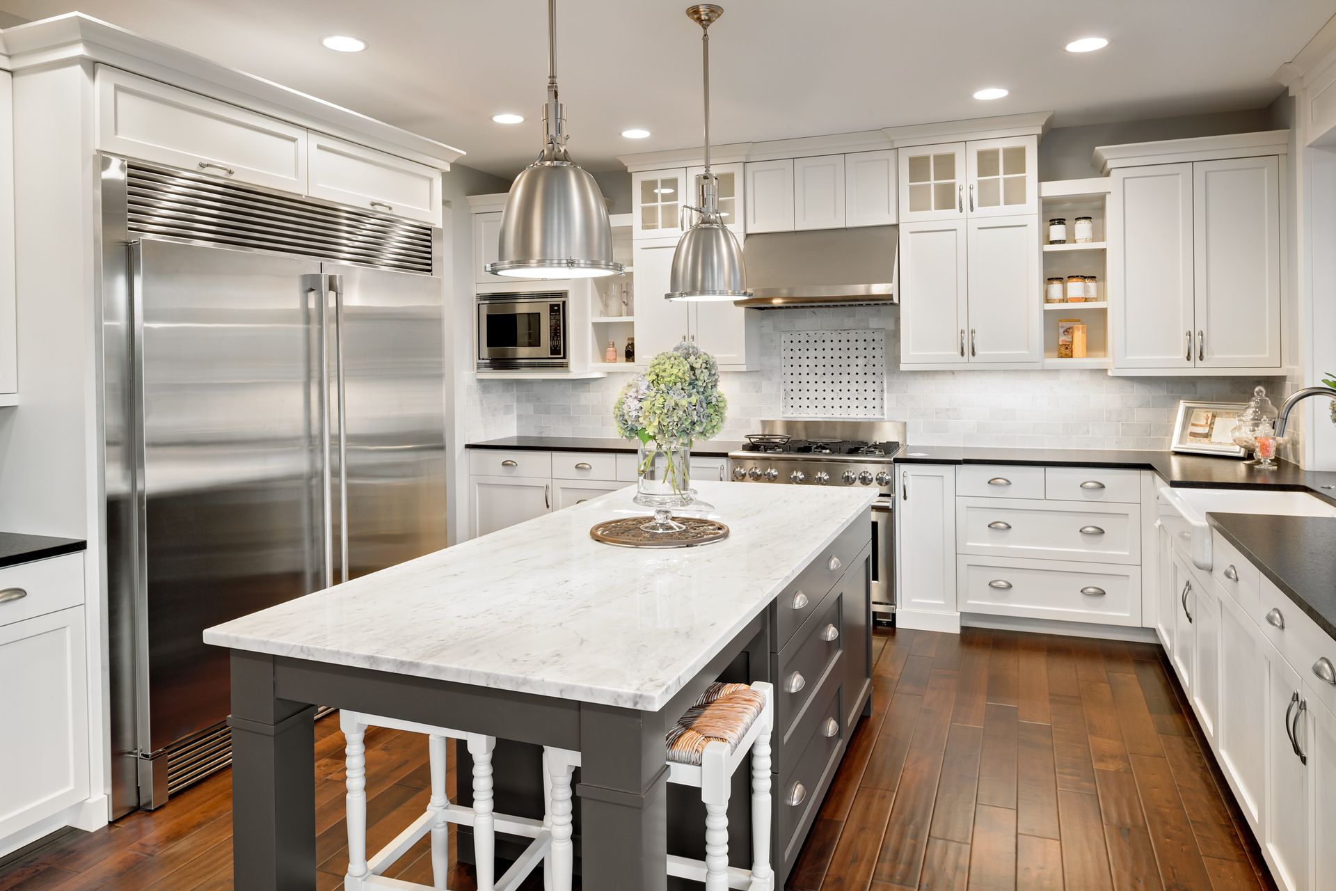 A kitchen with white cabinets and stainless steel appliances and a large island in the middle.