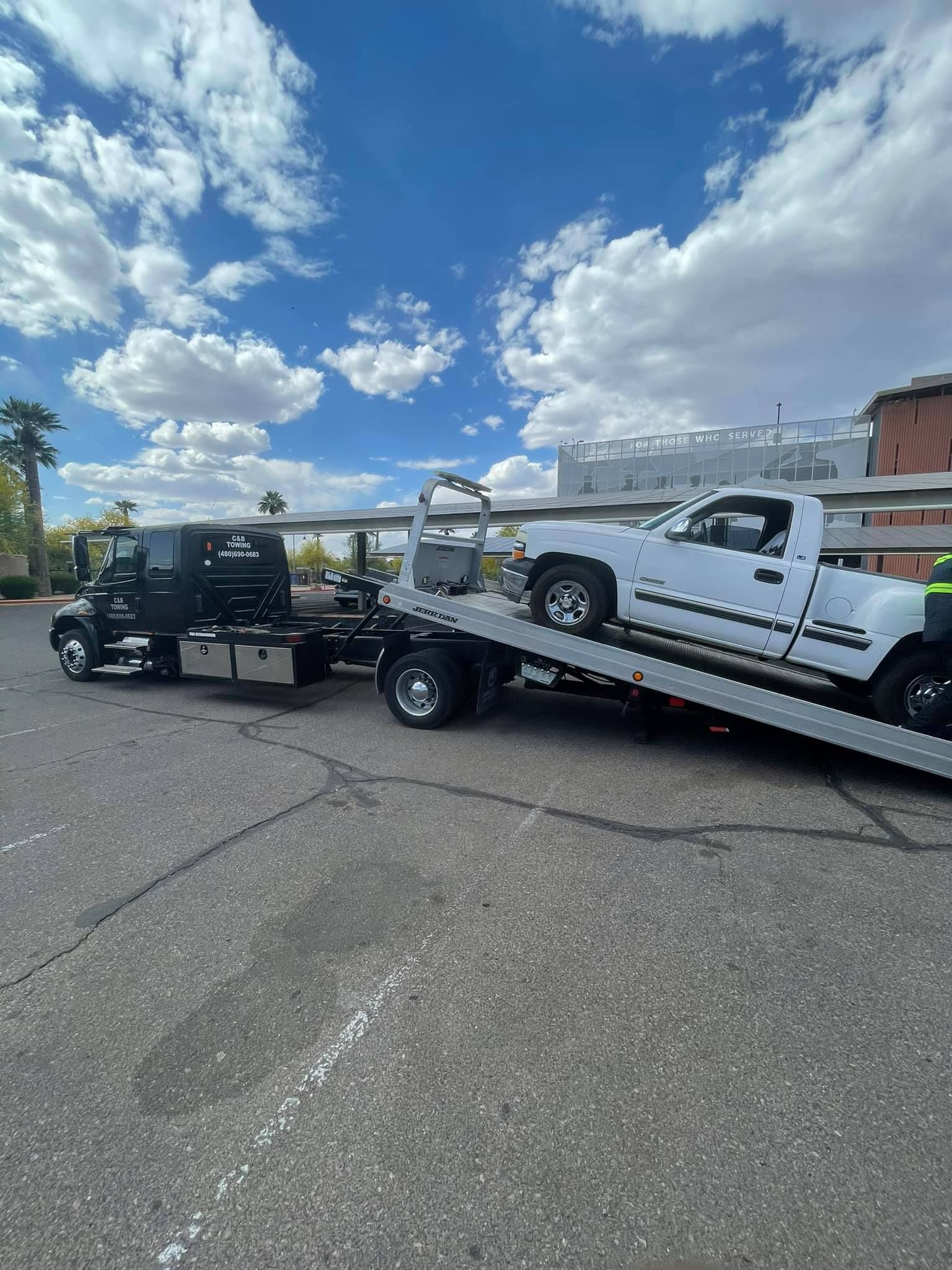 A white truck is being towed by a tow truck in a parking lot.