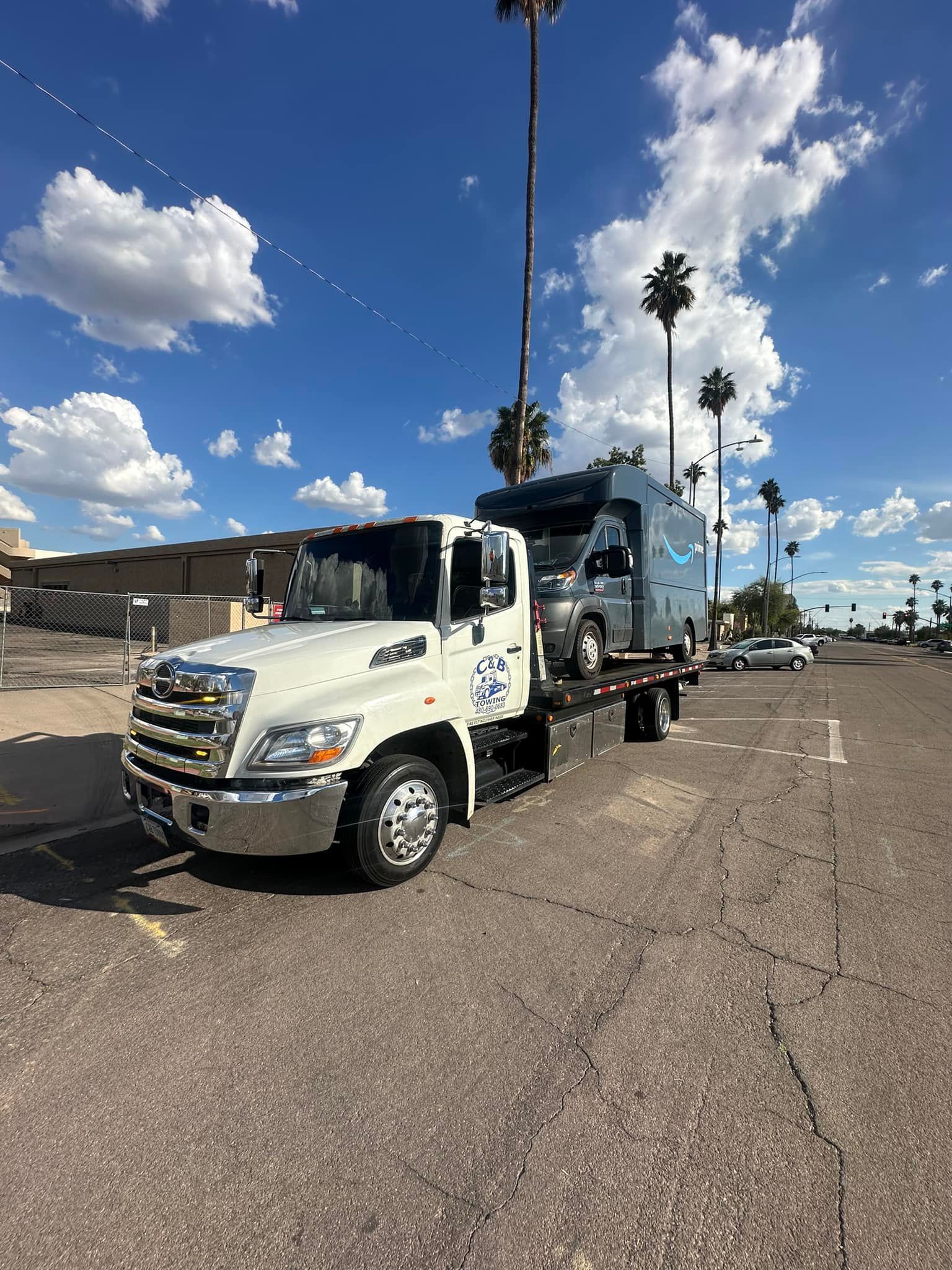 A white tow truck is towing a trailer down a street.