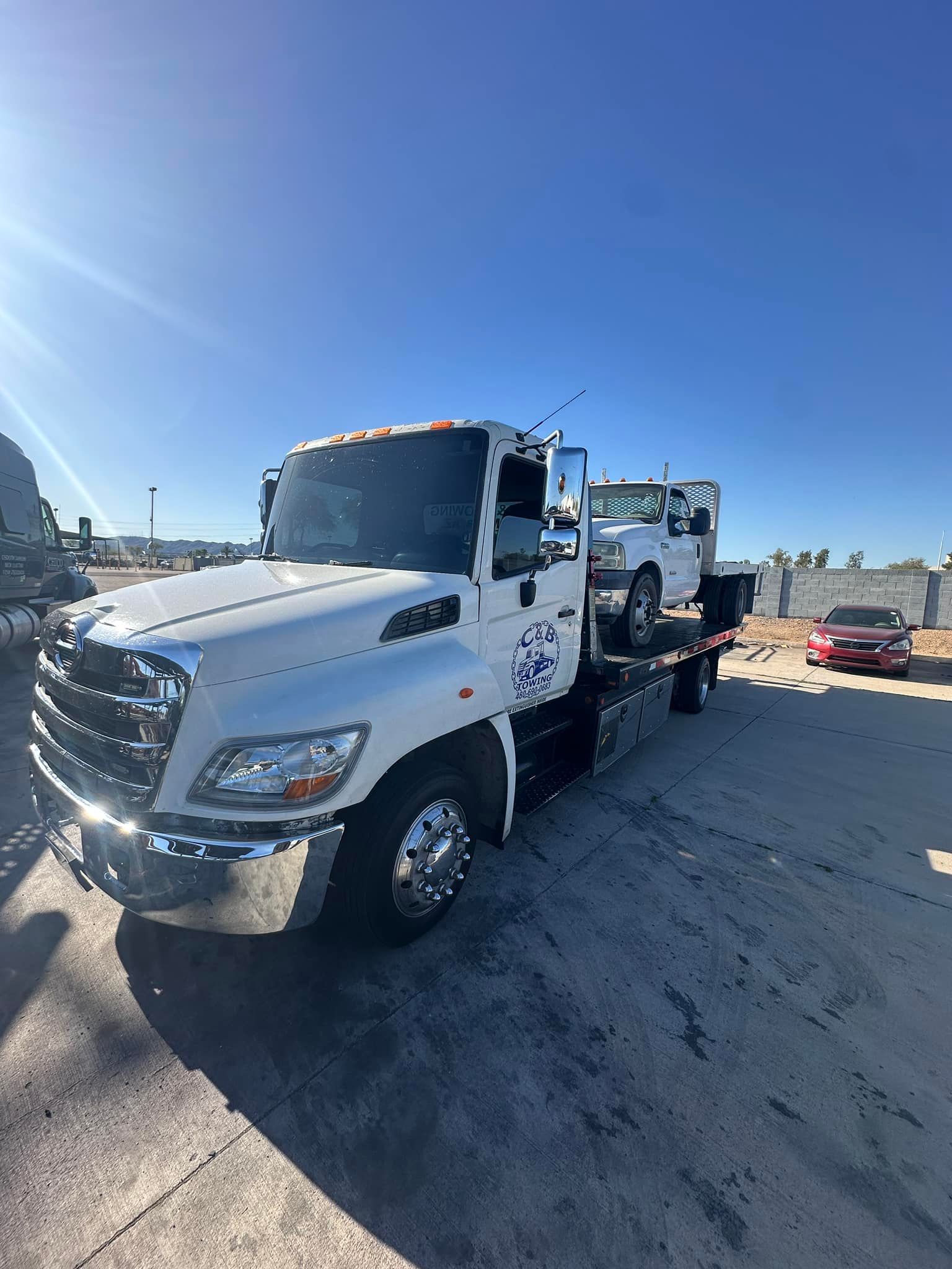 A white tow truck with two cars on the back is parked in a parking lot.