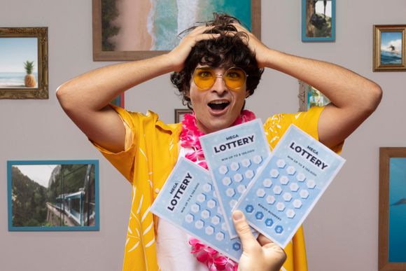 Una persona con camisa amarilla y gafas parece sorprendida mientras sostiene varios boletos de lotería para rascar.