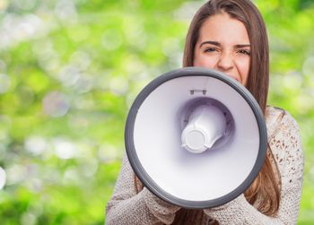 Una persona sostiene un megáfono frente a su boca con expresión concentrada, sobre un fondo verde difuminado.