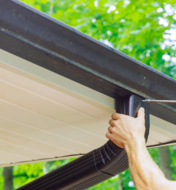 Person installing a black gutter downspout on a building.