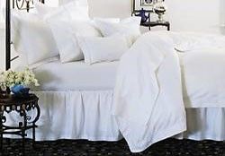 A bed with white sheets , pillows and a nightstand in a bedroom.