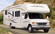 A white rv is driving down a road next to a mountain.