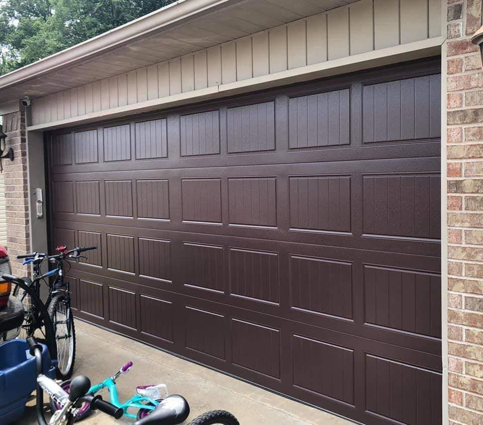 A dark brown, multi-paneled garage door on a brick home with bicycles parked in the driveway.