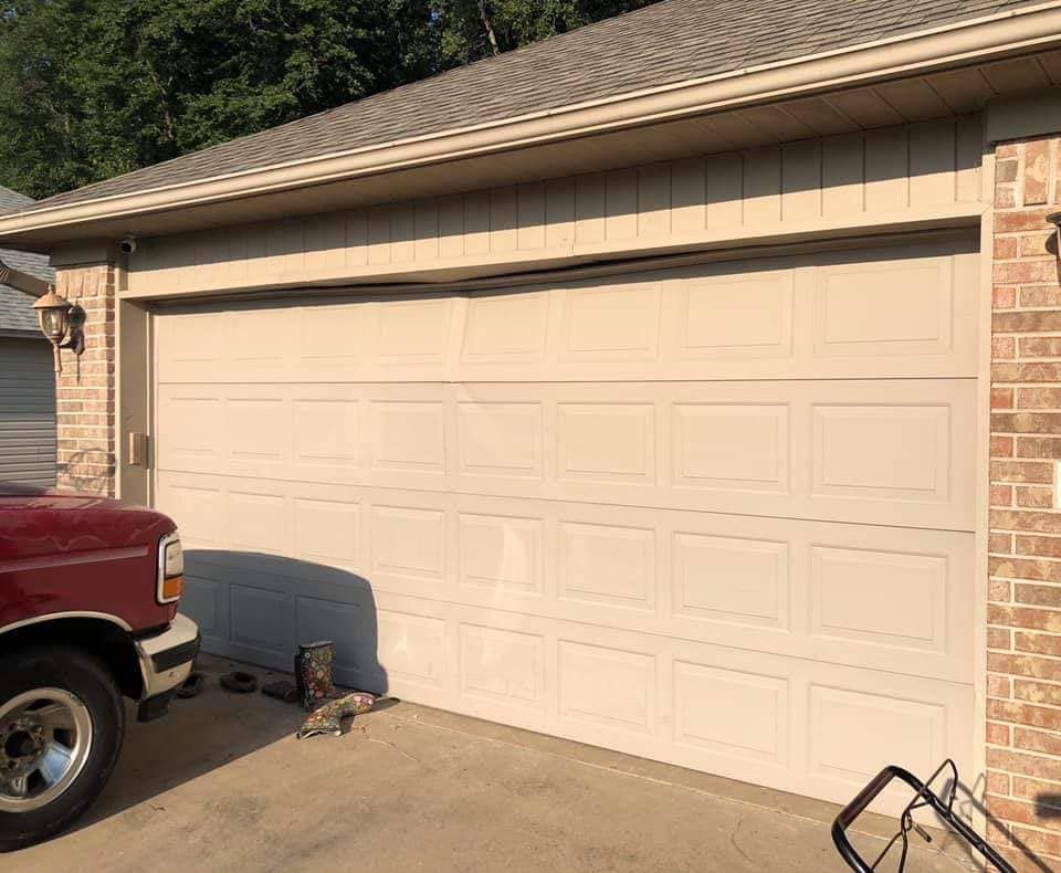 A beige garage door attached to a brick house, with the front of a red truck visible on the left.