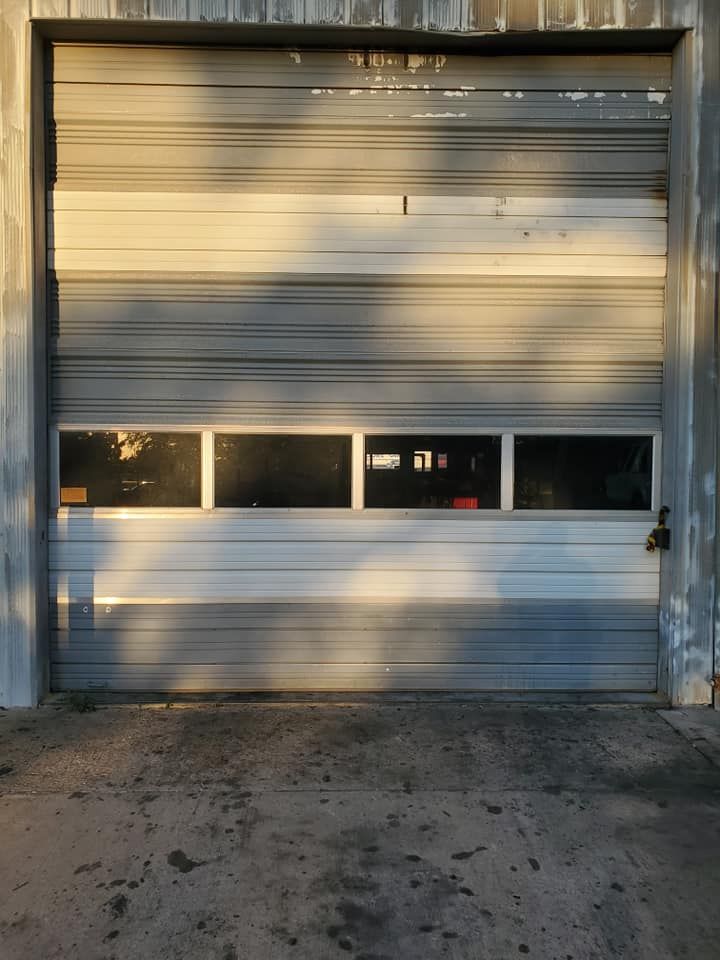 A gray industrial roll-up door with a row of four windows at eye level, framed by concrete walls.