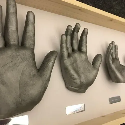 Three gray hands are displayed in a wooden frame.