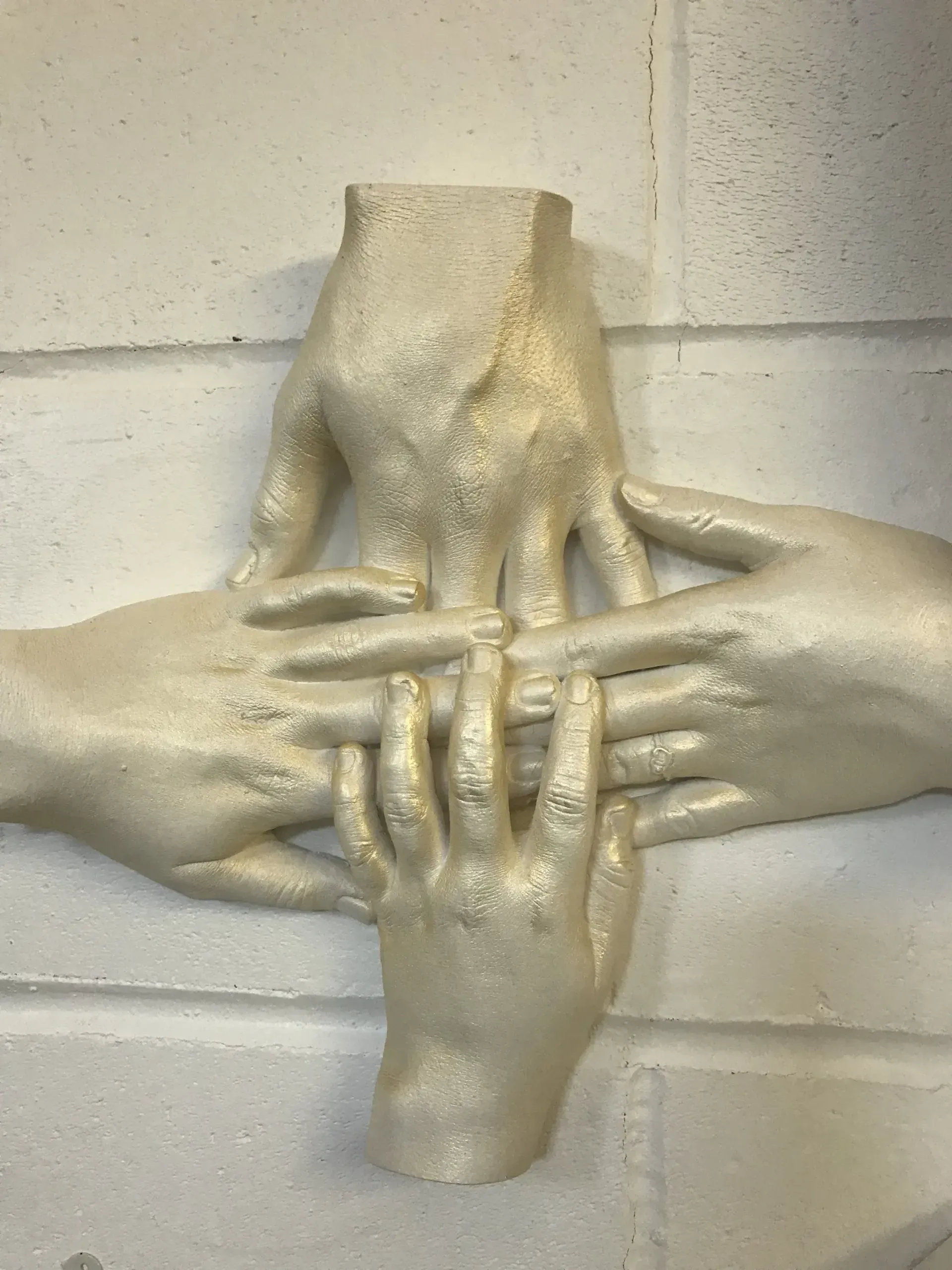 A statue of four hands holding each other on a white wall.