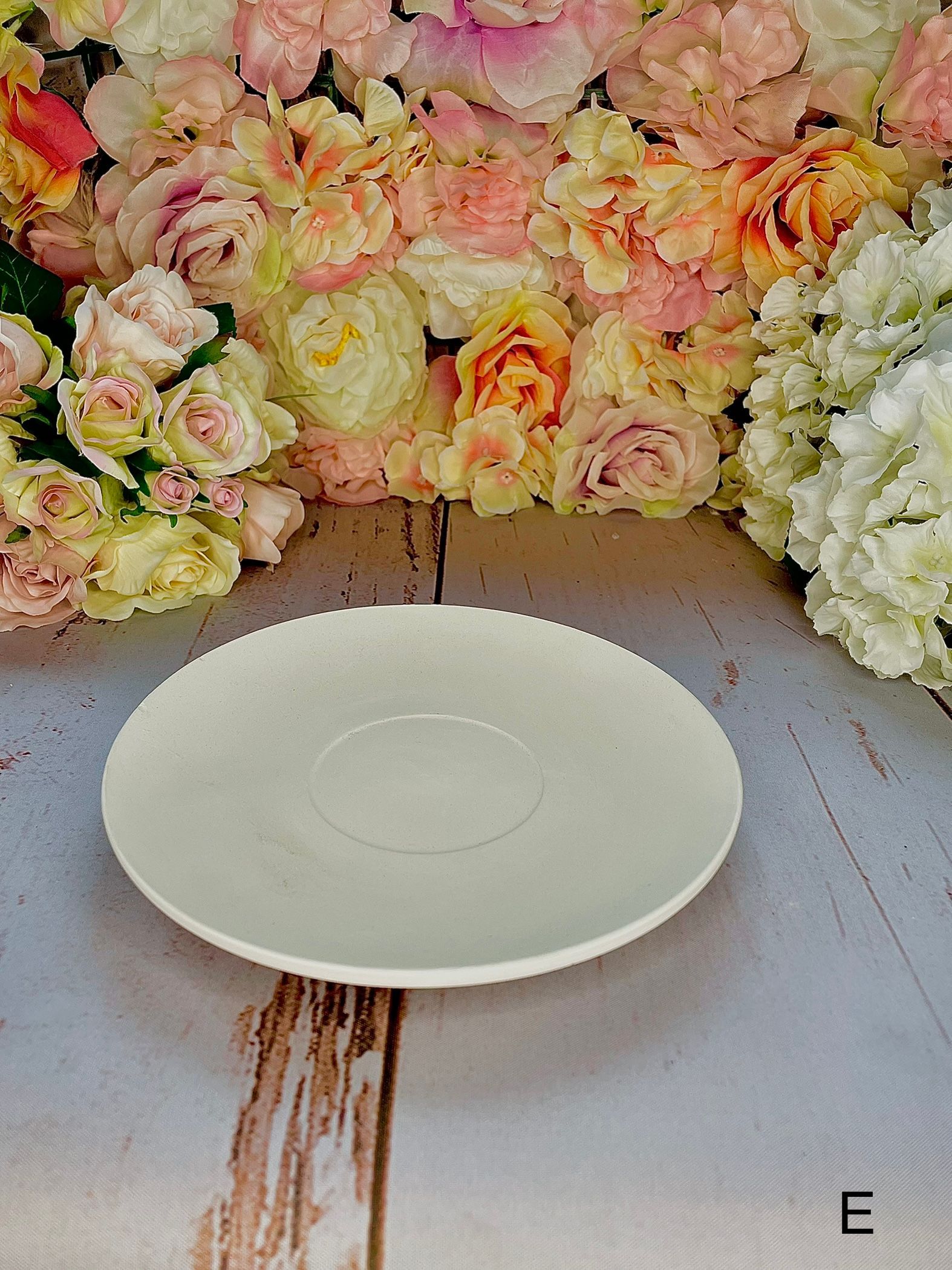 A white plate is sitting on a wooden table in front of a wall of flowers.