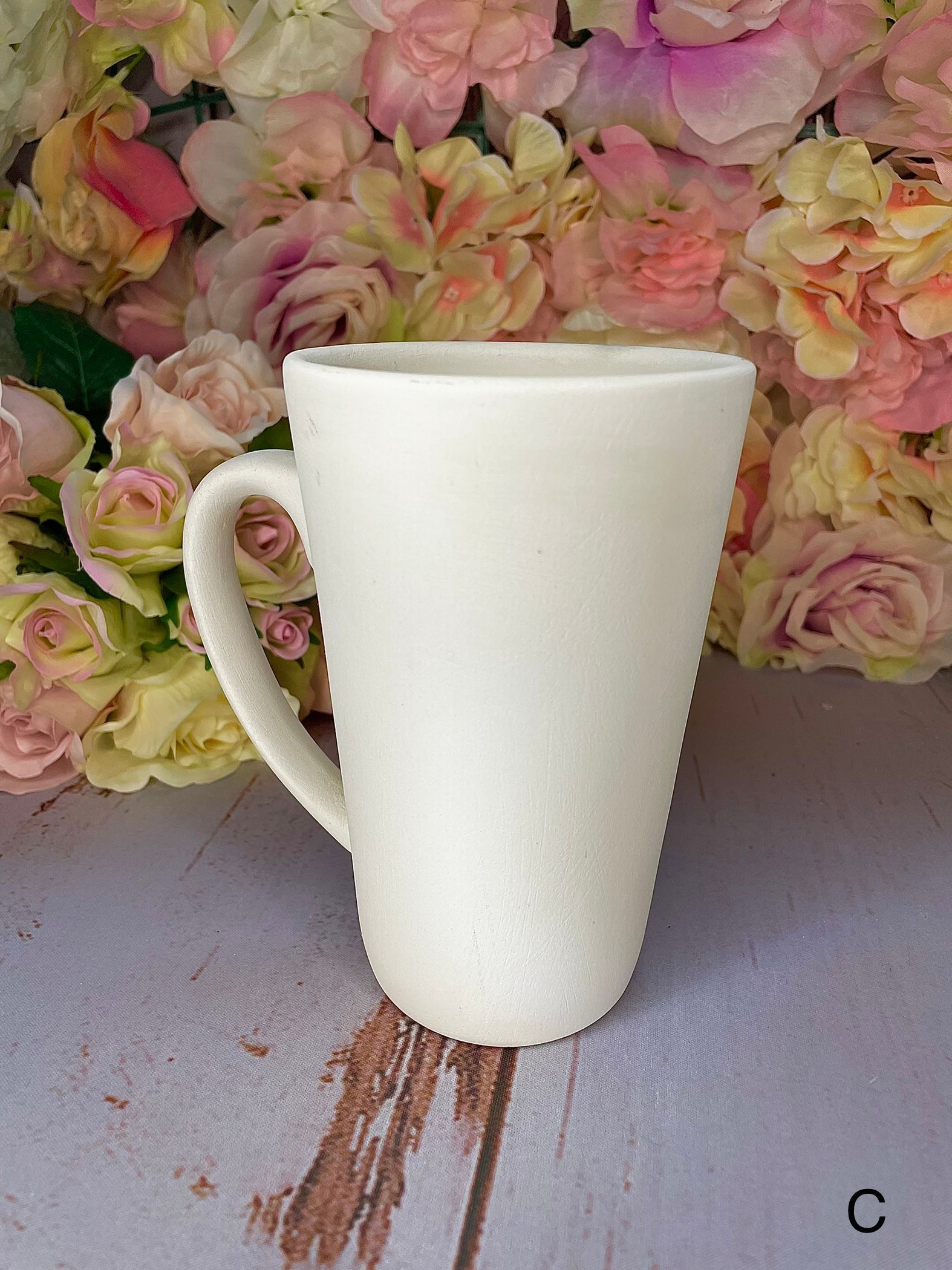 A white coffee mug is sitting on a table next to a bunch of pink roses.