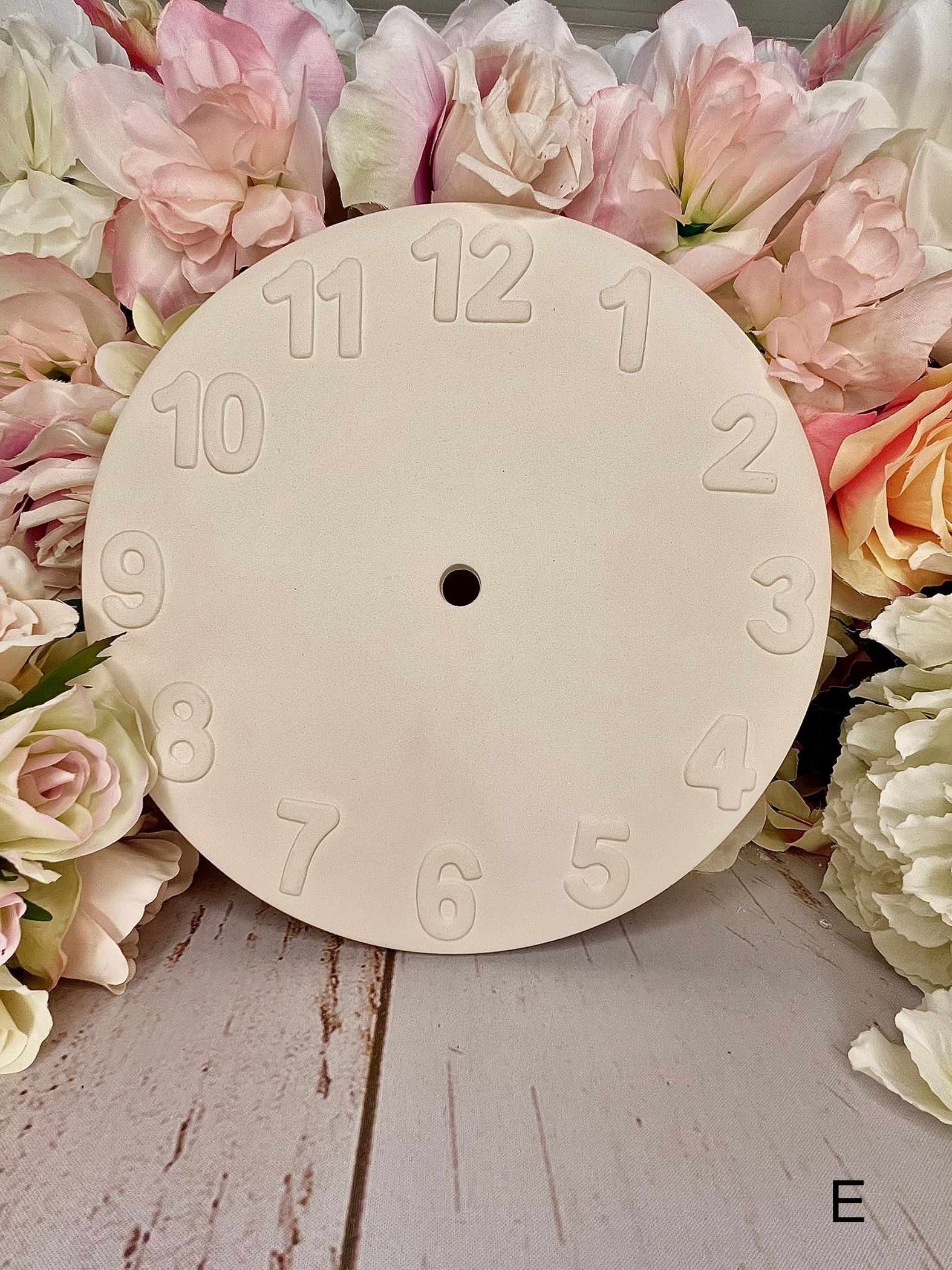 A clock face is sitting on a wooden table surrounded by flowers.