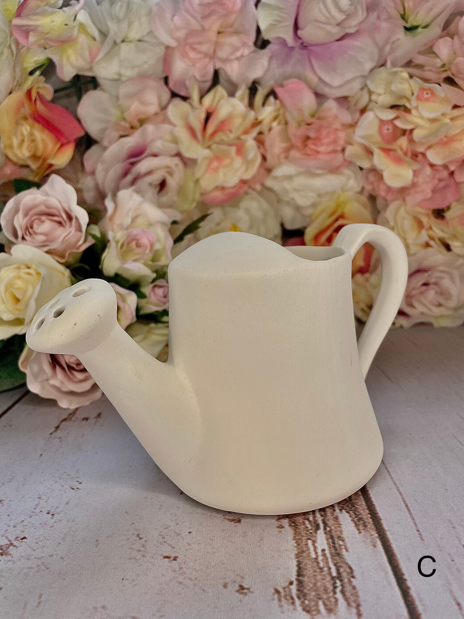 A white watering can is sitting in front of a bunch of flowers.